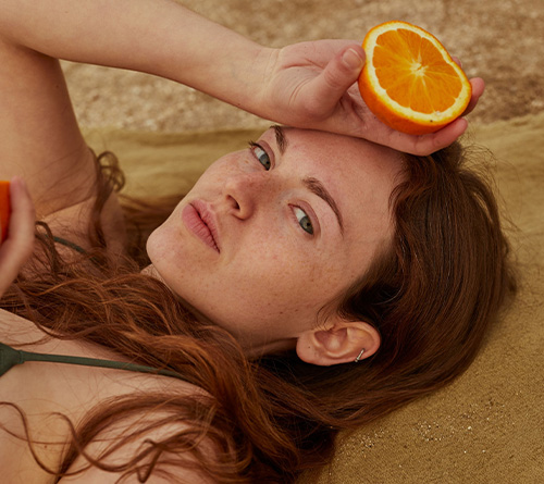 Close-up of red-haired girl holding half of an orange to her forehead